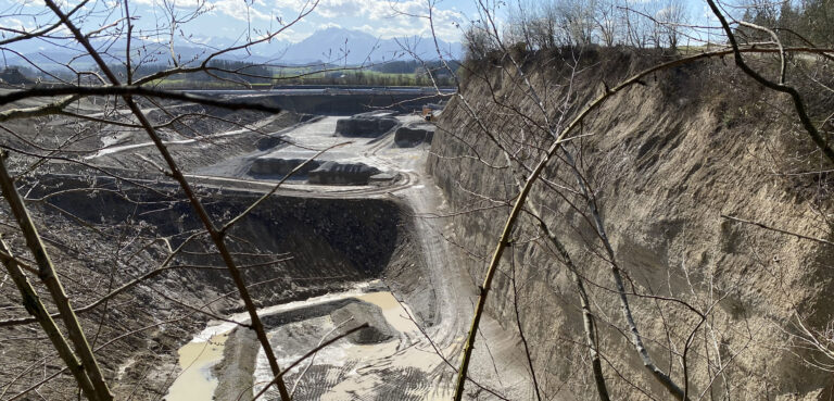 Kiesabbau und Auffüllung. Blick von oben in die Kiesgrube. Baggerpisten durchziehen die Grube. An der tiefsten Stelle staut sich das Wasser.