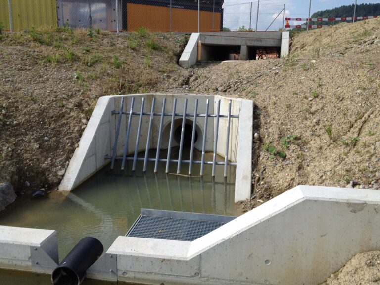 Dienstleistung Hochwasserschutz: Einlaufbauwerk mit Rechen, damit die Röhre nicht verstopft wird. Umgebung noch spärlich begrünt.